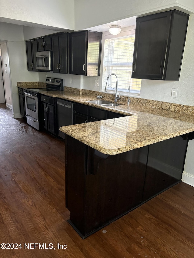 kitchen featuring kitchen peninsula, dark hardwood / wood-style flooring, light stone counters, stainless steel appliances, and sink