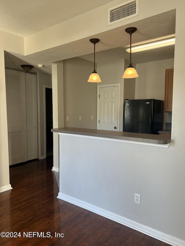 kitchen with dark wood-type flooring, black refrigerator, hanging light fixtures, and a textured ceiling