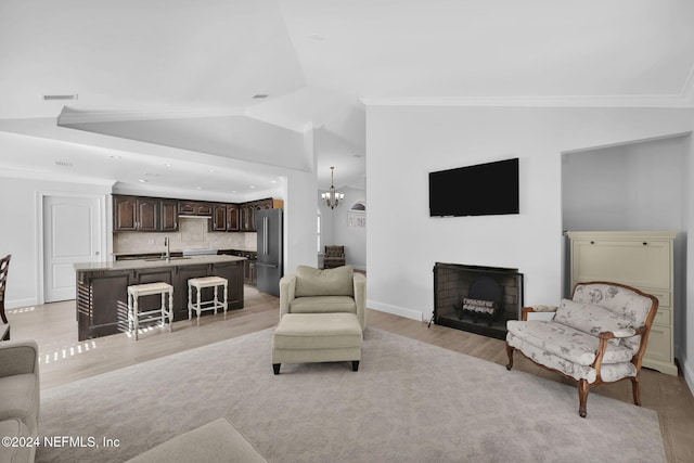 living room featuring light wood-type flooring, ornamental molding, sink, a chandelier, and lofted ceiling