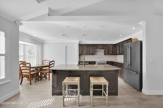 kitchen featuring backsplash, ornamental molding, a kitchen island with sink, and stainless steel refrigerator