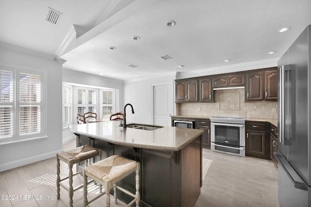 kitchen with sink, stainless steel appliances, backsplash, an island with sink, and light wood-type flooring