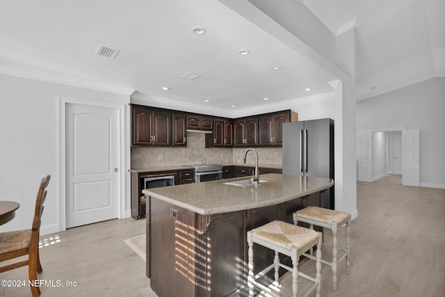 kitchen featuring sink, an island with sink, light hardwood / wood-style floors, light stone counters, and dark brown cabinetry