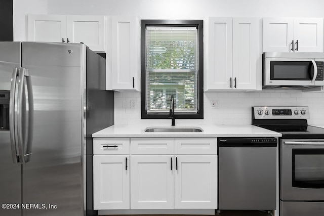 kitchen with light stone countertops, white cabinetry, sink, stainless steel appliances, and backsplash