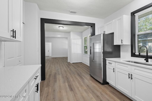 kitchen featuring stainless steel refrigerator with ice dispenser, light wood-type flooring, a textured ceiling, sink, and white cabinets