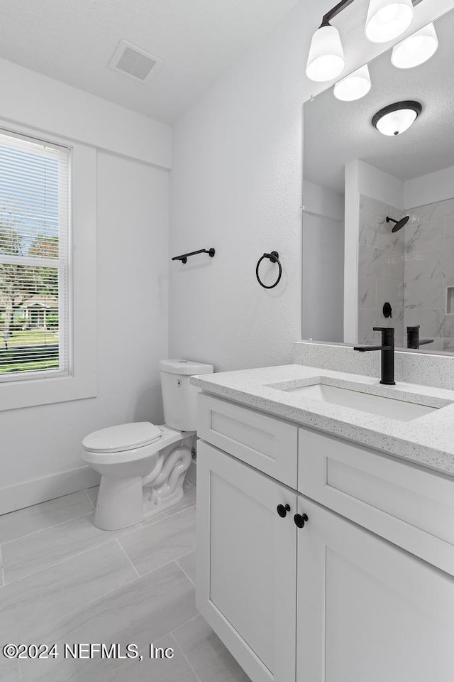 bathroom with a tile shower, vanity, and toilet