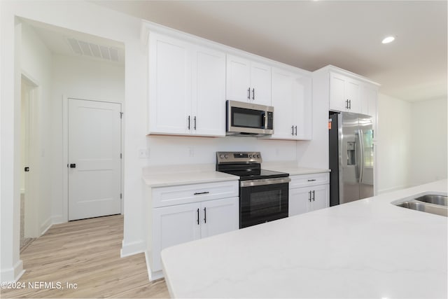 kitchen featuring light stone counters, white cabinets, stainless steel appliances, and light wood-type flooring