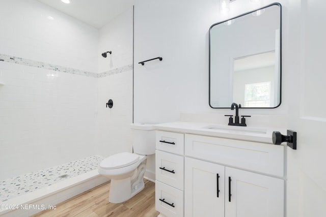 bathroom with a tile shower, hardwood / wood-style floors, vanity, and toilet