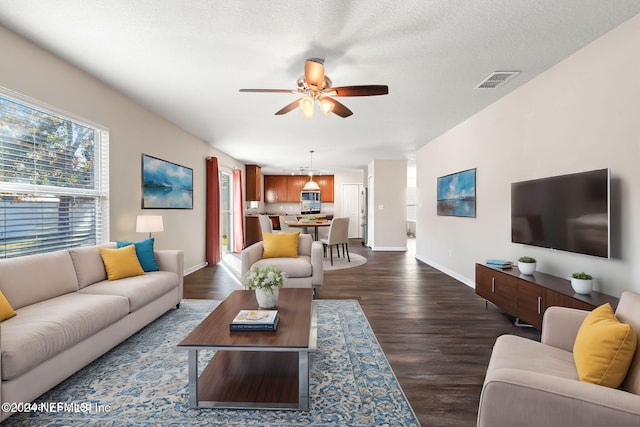 living room featuring ceiling fan, dark wood-type flooring, and a textured ceiling