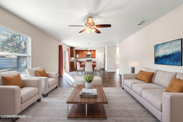 living room with a textured ceiling, light hardwood / wood-style flooring, and ceiling fan