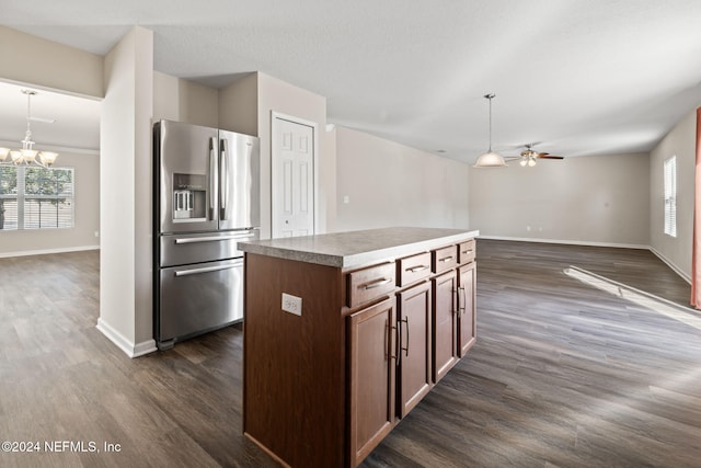 kitchen with stainless steel fridge, ceiling fan with notable chandelier, decorative light fixtures, dark hardwood / wood-style floors, and a kitchen island