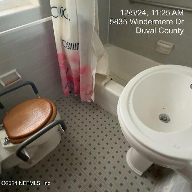 bathroom featuring shower / bath combo, toilet, and tile walls