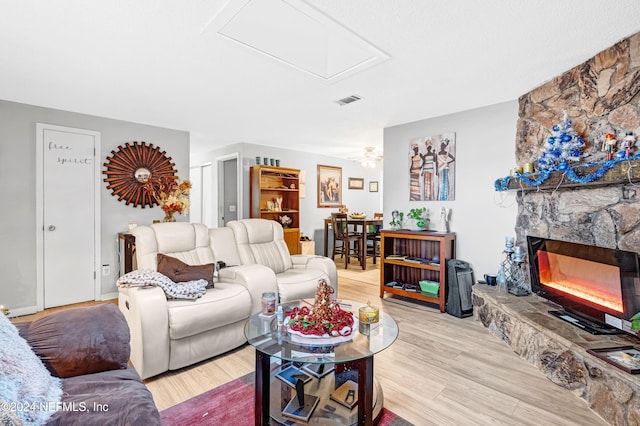 living room with ceiling fan, a stone fireplace, and light wood-type flooring