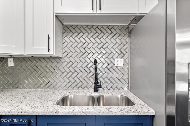 kitchen with backsplash, white cabinetry, light stone counters, and sink