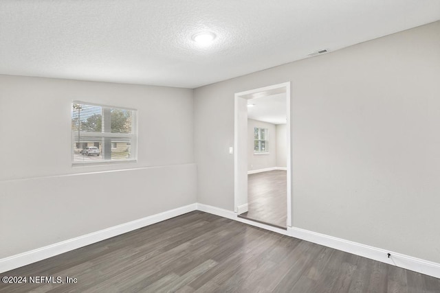 empty room with dark hardwood / wood-style flooring, a textured ceiling, and vaulted ceiling