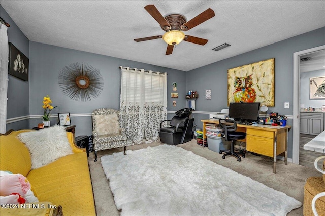 carpeted home office with ceiling fan and a textured ceiling