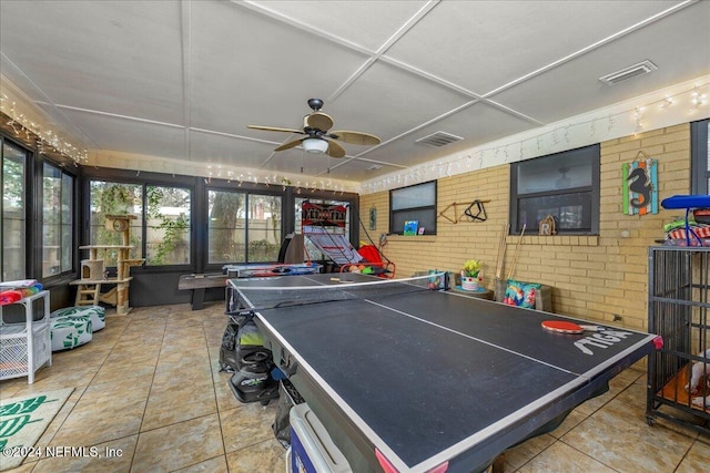 recreation room with ceiling fan, tile patterned flooring, and brick wall