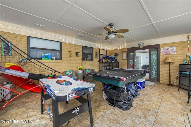 recreation room featuring tile patterned floors, ceiling fan, and brick wall