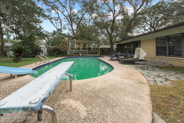 view of pool with a diving board, a patio area, and a water slide