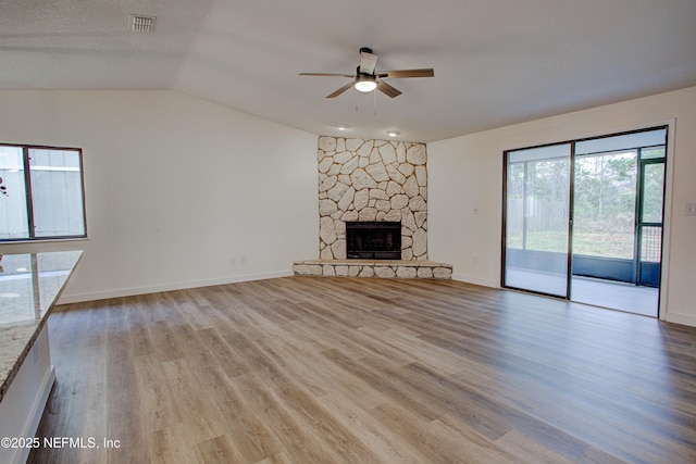 unfurnished living room with visible vents, light wood-style flooring, a ceiling fan, vaulted ceiling, and a stone fireplace