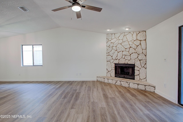 unfurnished living room with visible vents, a ceiling fan, lofted ceiling, wood finished floors, and a stone fireplace