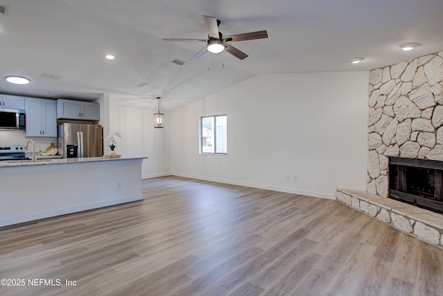 unfurnished living room featuring light wood finished floors, baseboards, lofted ceiling, ceiling fan, and a stone fireplace