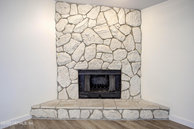 details featuring a stone fireplace, baseboards, and wood finished floors