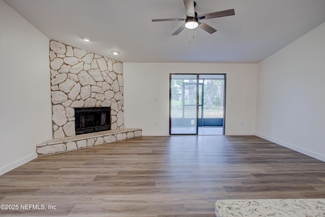 unfurnished living room featuring baseboards, a ceiling fan, lofted ceiling, wood finished floors, and a stone fireplace