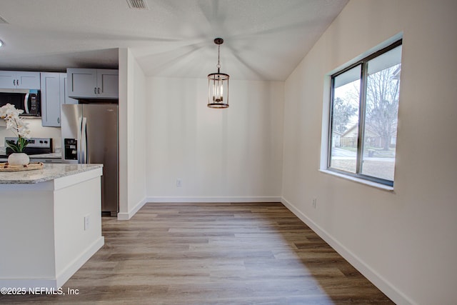 kitchen with light stone counters, stainless steel appliances, hanging light fixtures, light wood-style flooring, and baseboards