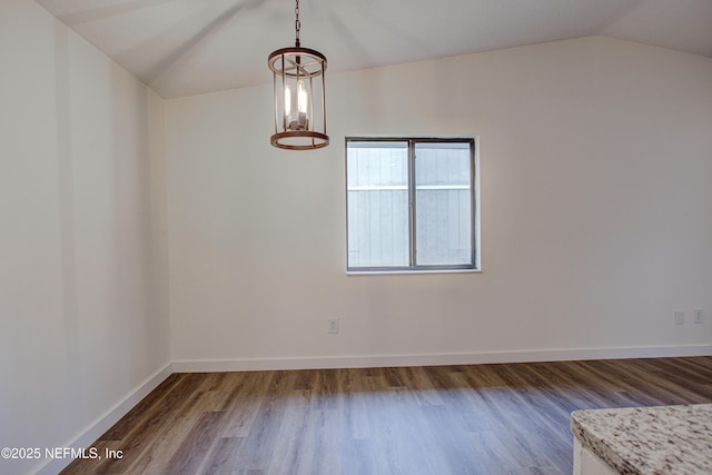 unfurnished dining area featuring baseboards, vaulted ceiling, and wood finished floors