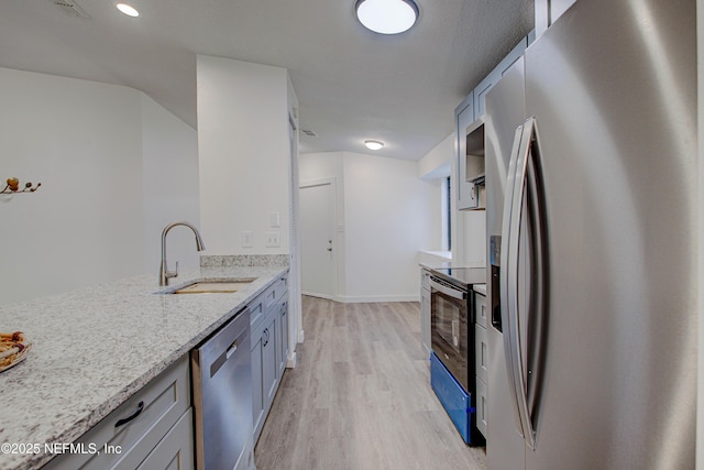 kitchen with light wood finished floors, appliances with stainless steel finishes, a sink, light stone countertops, and baseboards