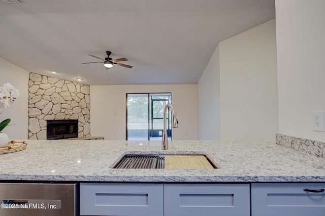 kitchen featuring ceiling fan, light stone counters, open floor plan, a fireplace, and a sink