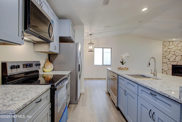 kitchen featuring light stone counters, light wood-style flooring, appliances with stainless steel finishes, vaulted ceiling, and a sink