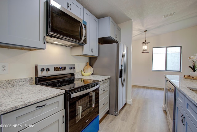 kitchen featuring light wood finished floors, visible vents, appliances with stainless steel finishes, light stone countertops, and a textured ceiling