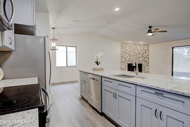 kitchen featuring light wood-style flooring, light stone counters, stainless steel appliances, gray cabinetry, and a sink