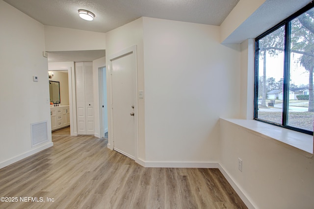 interior space with light wood-type flooring, visible vents, a textured ceiling, and baseboards