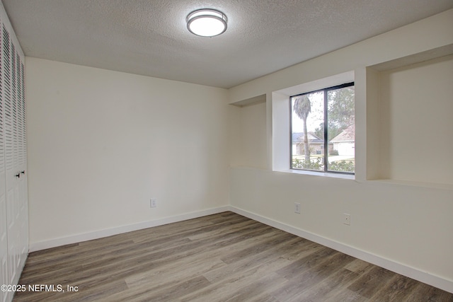 empty room featuring a textured ceiling, baseboards, and wood finished floors