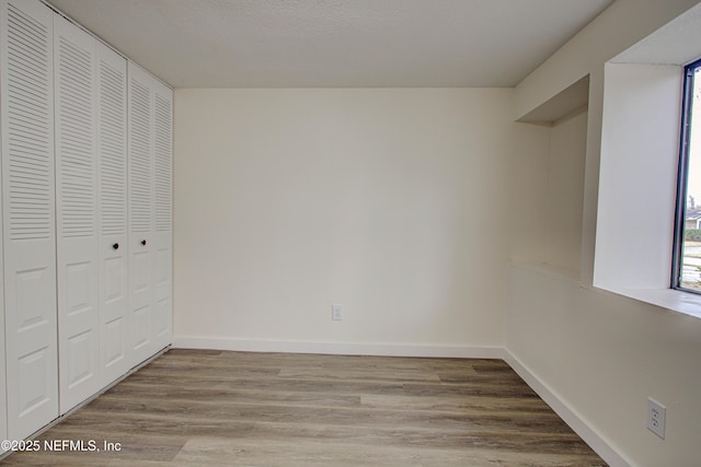 unfurnished bedroom with a closet, baseboards, wood finished floors, and multiple windows