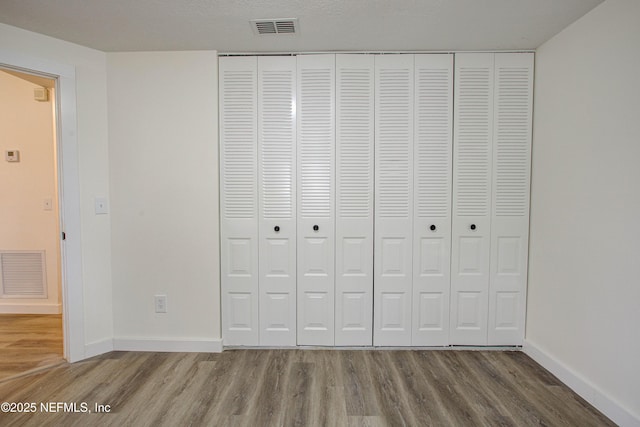 unfurnished bedroom featuring a closet, wood finished floors, visible vents, and baseboards