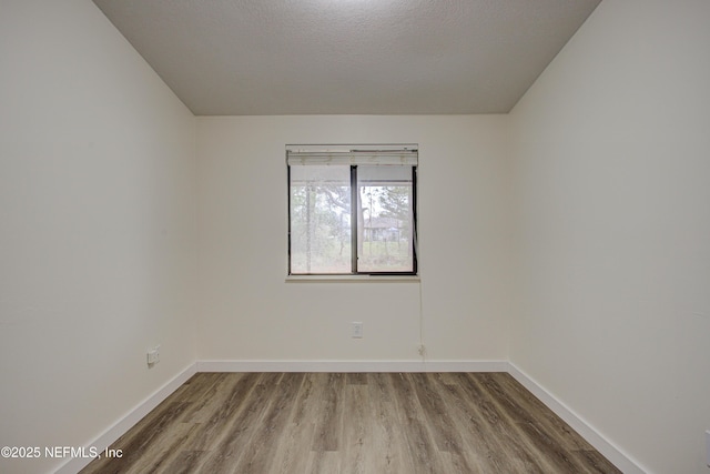 spare room with a textured ceiling, baseboards, and wood finished floors