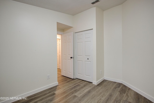 unfurnished bedroom with wood finished floors, visible vents, and baseboards