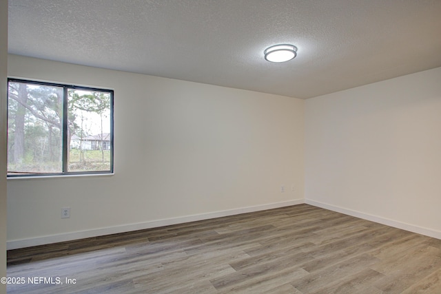 empty room featuring a textured ceiling, baseboards, and wood finished floors