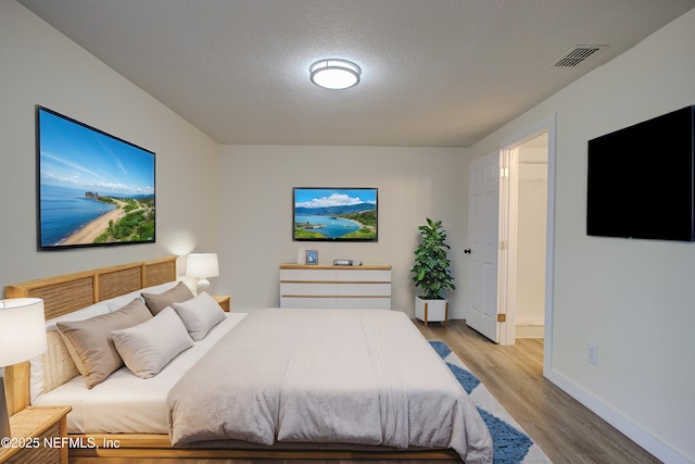 bedroom featuring baseboards, visible vents, a textured ceiling, and light wood finished floors