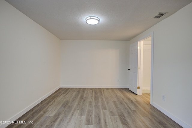 spare room with a textured ceiling, wood finished floors, visible vents, and baseboards