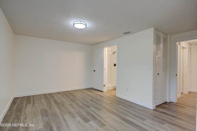 spare room with light wood-type flooring, visible vents, a textured ceiling, and baseboards