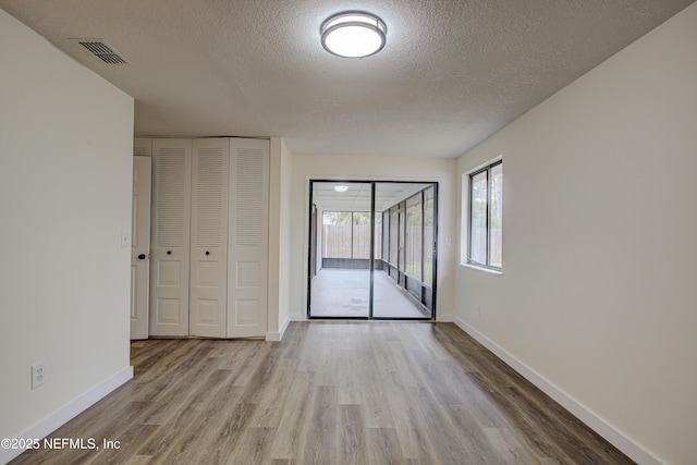 unfurnished room with visible vents, a textured ceiling, baseboards, and wood finished floors