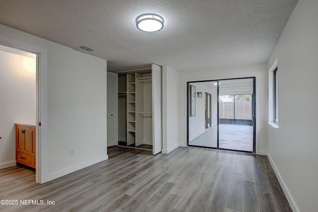 unfurnished bedroom featuring access to outside, visible vents, baseboards, and wood finished floors