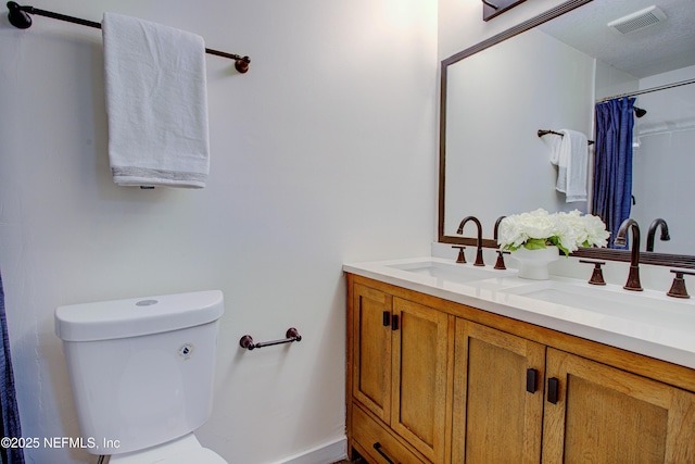 bathroom with toilet, double vanity, visible vents, and a sink