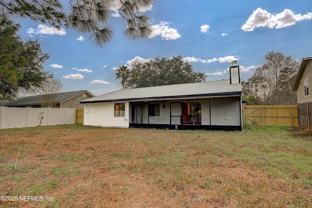 rear view of house featuring a lawn, a chimney, and a fenced backyard