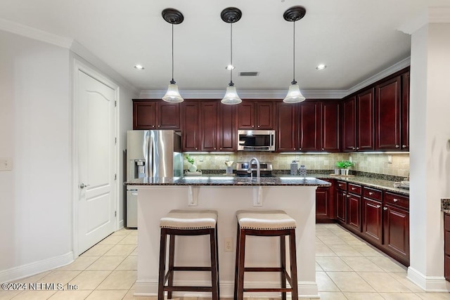 kitchen with decorative backsplash, stainless steel appliances, light tile patterned floors, a center island with sink, and dark stone countertops