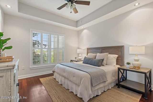 bedroom with a tray ceiling, ceiling fan, and dark hardwood / wood-style flooring